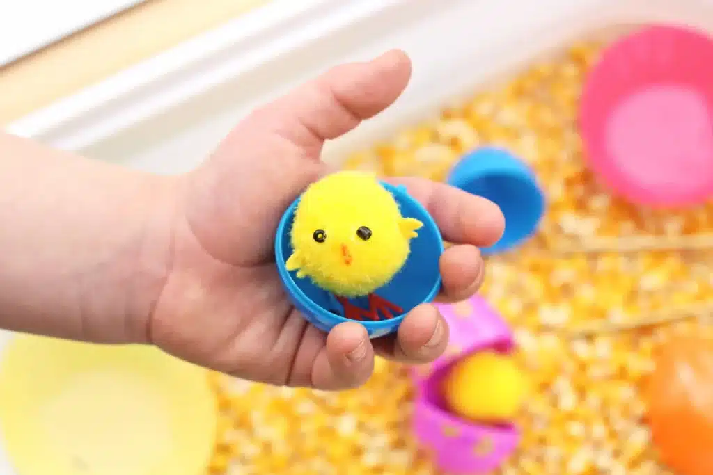 Chick Hatch Sensory Bin - Cultivating Brilliant Minds a kid holding an easter egg with a chick inside