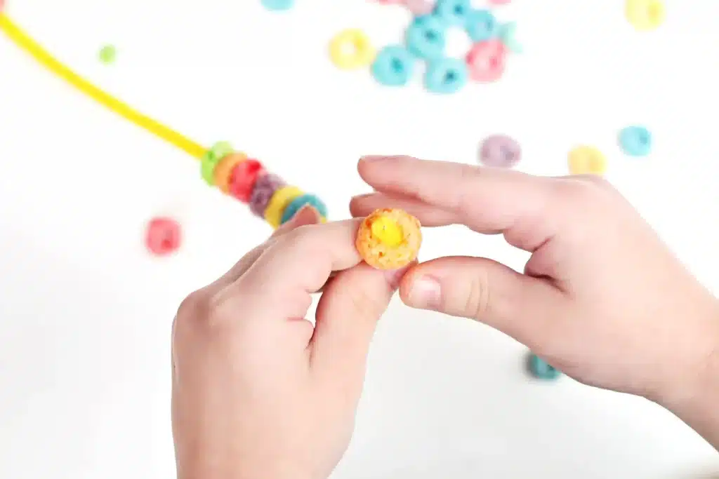 Froot Loops Rainbow Snack - Cultivating Brilliant Minds a child threading froot loops on a pipe cleaner in rainbow order