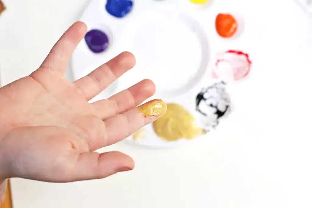 Paper Plate Pot of Gold with Fingerprint Coins - Cultivating Brilliant Minds a kid's hand with gold paint on the pointer finger