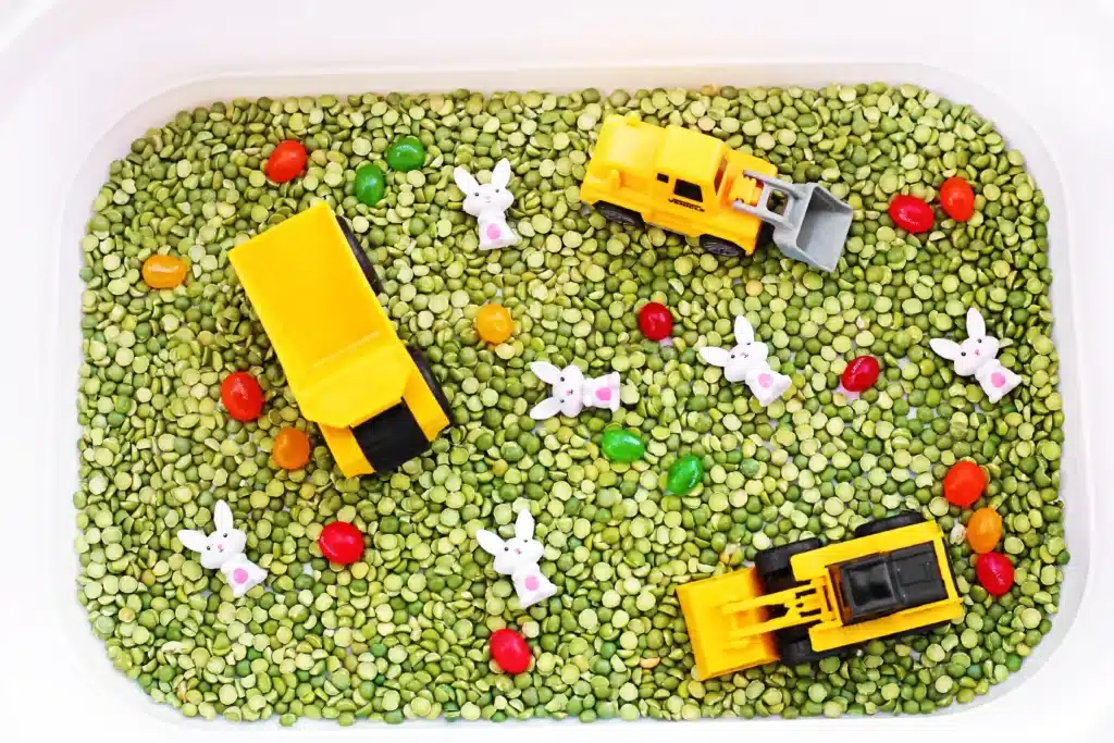 Easter Construction Sensory Bin - Cultivating Brilliant Minds an easter construction sensory bin made of split peas, jelly beans, toy bunnies, and construction vehicles