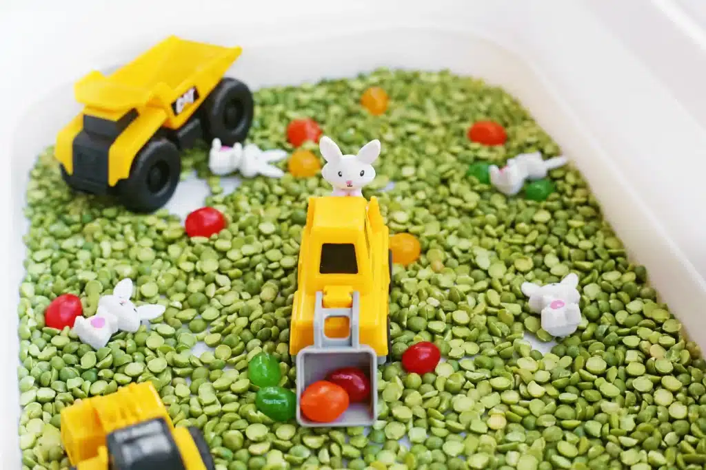 Easter Construction Sensory Bin - Cultivating Brilliant Minds an easter construction sensory bin made of split peas, jelly beans, toy bunnies, and construction vehicles