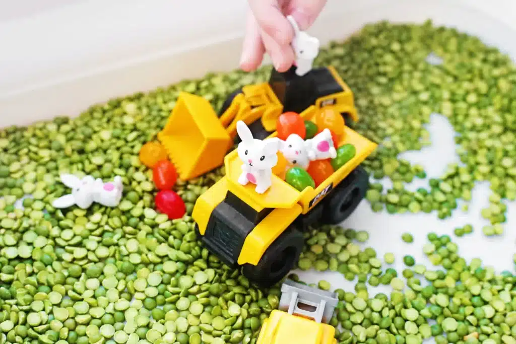 Easter Construction Sensory Bin - Cultivating Brilliant Minds an easter construction sensory bin made of split peas, jelly beans, toy bunnies, and construction vehicles