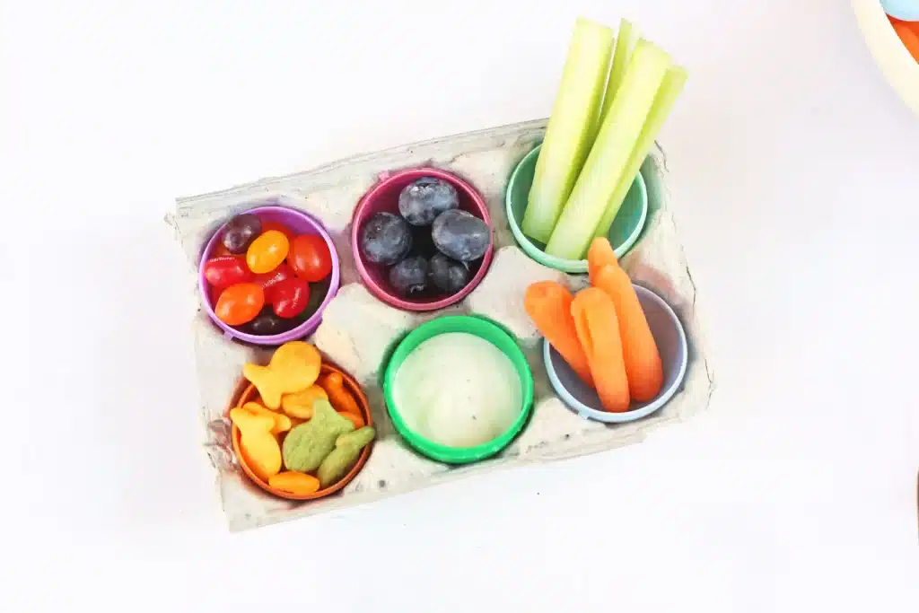 Easter Egg Snack Tray - Cultivating Brilliant Minds an easter egg snack tray with an egg carton with plastic eggs inside and the eggs have jelly beans, blueberries, celery, carrots, goldfish, and ranch dressing inside
