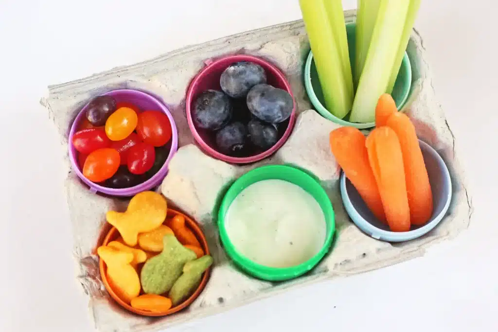 Easter Egg Snack Tray - Cultivating Brilliant Minds an easter egg snack tray with an egg carton with plastic eggs inside and the eggs have jelly beans, blueberries, celery, carrots, goldfish, and ranch dressing inside