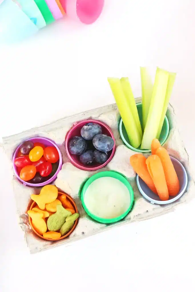 Easter Egg Snack Tray - Cultivating Brilliant Minds an easter egg snack tray with an egg carton with plastic eggs inside and the eggs have jelly beans, blueberries, celery, carrots, goldfish, and ranch dressing inside