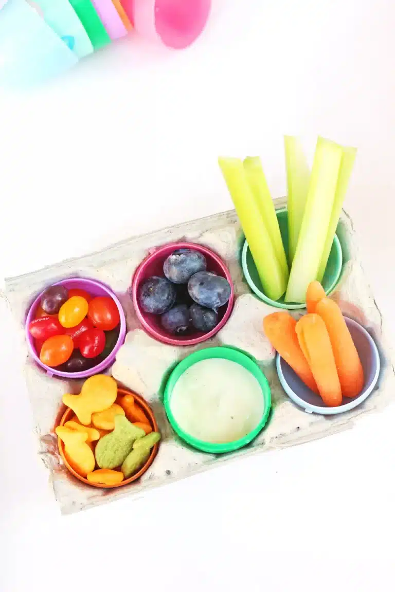 an easter egg snack tray with an egg carton with plastic eggs inside and the eggs have jelly beans, blueberries, celery, carrots, goldfish, and ranch dressing inside