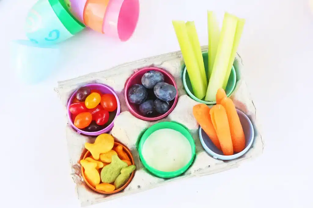 Easter Egg Snack Tray - Cultivating Brilliant Minds an easter egg snack tray with an egg carton with plastic eggs inside and the eggs have jelly beans, blueberries, celery, carrots, goldfish, and ranch dressing inside