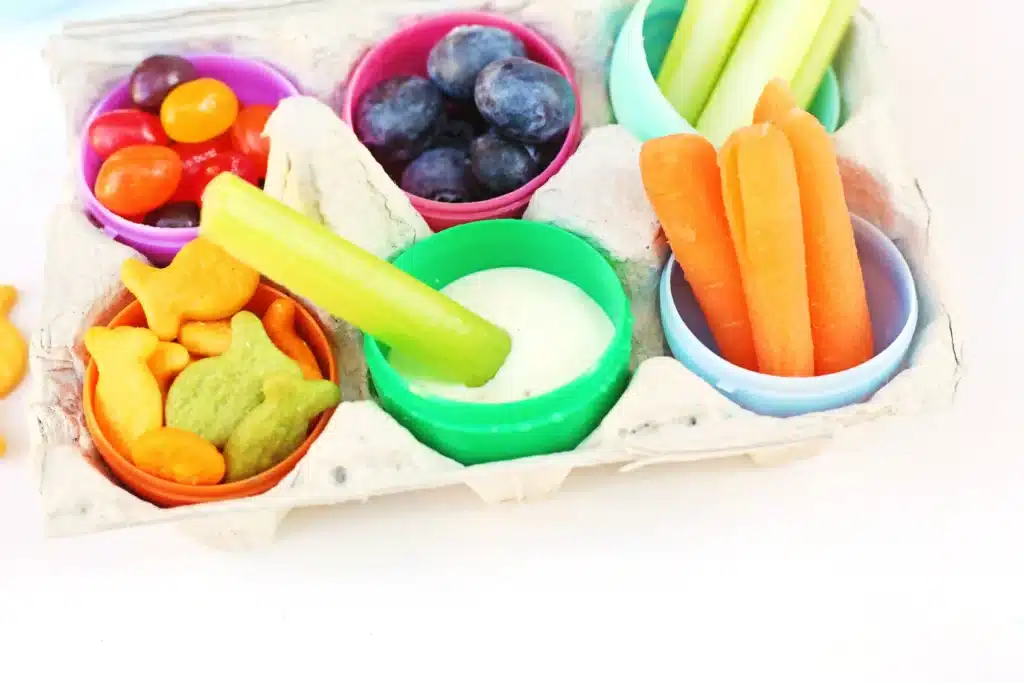 Easter Egg Snack Tray - Cultivating Brilliant Minds an easter egg snack tray with an egg carton with plastic eggs inside and the eggs have jelly beans, blueberries, celery, carrots, goldfish, and ranch dressing inside