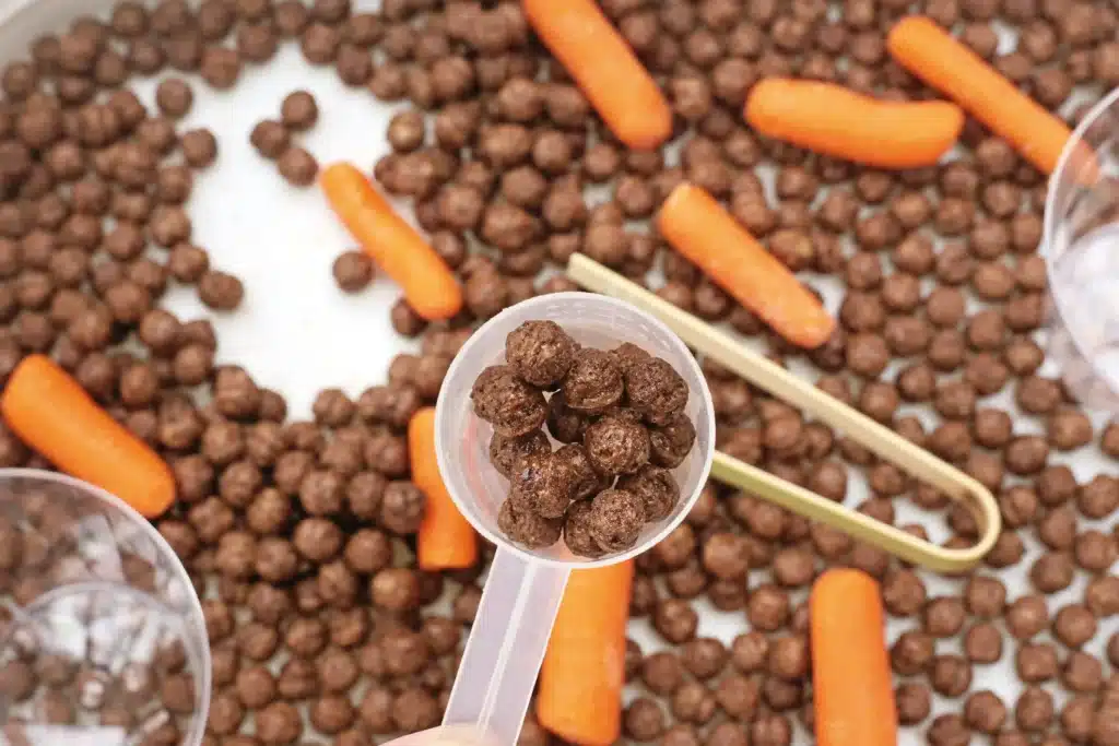 Edible Carrot Patch Sensory Bin For Spring - Cultivating Brilliant Minds a measuring cup withe cocoa puffs inside