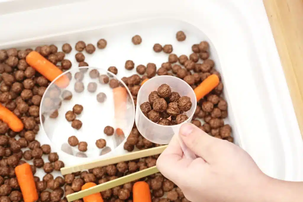 Edible Carrot Patch Sensory Bin For Spring - Cultivating Brilliant Minds a kid with a measuring cup full of cocoa puffs