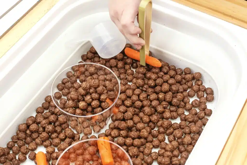 Edible Carrot Patch Sensory Bin For Spring - Cultivating Brilliant Minds a kid using tongs to pick up a carrot