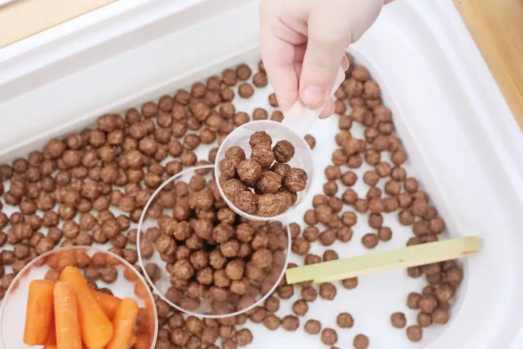 Edible Carrot Patch Sensory Bin For Spring - Cultivating Brilliant Minds a measuring cup withe cocoa puffs inside