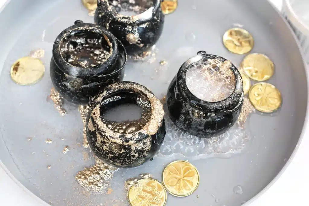 Fizzy Pot of Gold Experiment - Cultivating Brilliant Minds fizzy pot of gold experiment that uses cauldron pots, gold glitter, baking soda, and vinegar to create a "volcano"