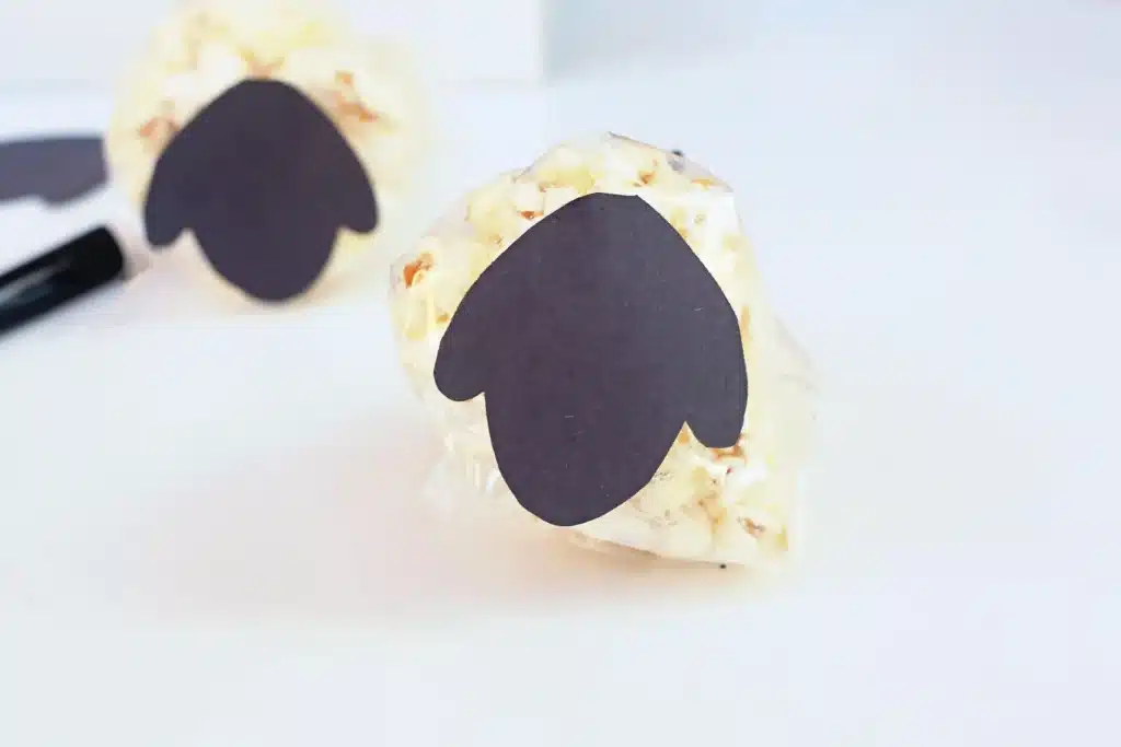 Sheep Popcorn Balls - Cultivating Brilliant Minds a popcorn ball in a bag with a sheep head made out of black construction paper taped on