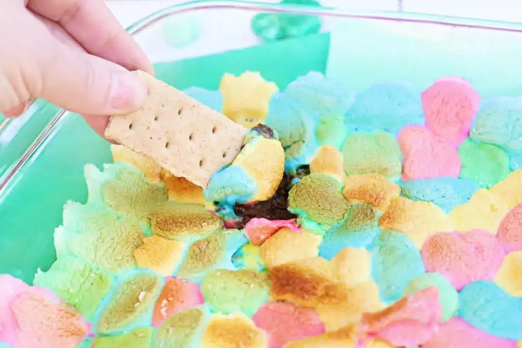 Lucky Charms S'mores Dip - Cultivating Brilliant Minds a graham cracker dipped into a lucky charms s'mores dip that has melted chocolate a lucky charm marshmallows