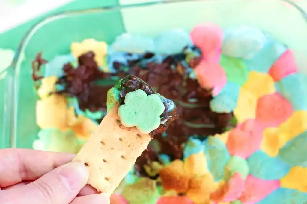 Lucky Charms S'mores Dip - Cultivating Brilliant Minds a graham cracker dipped into a lucky charms s'mores dip that has melted chocolate a lucky charm marshmallows