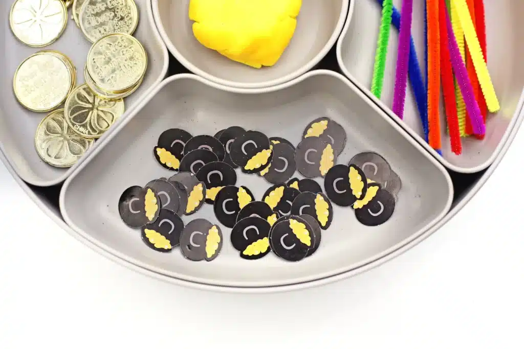 Pot of Gold Playdough Tray - Cultivating Brilliant Minds a tray with yellow playdough, colored pipe cleaners, gold coins, black cauldron pots, and pots of gold confetti