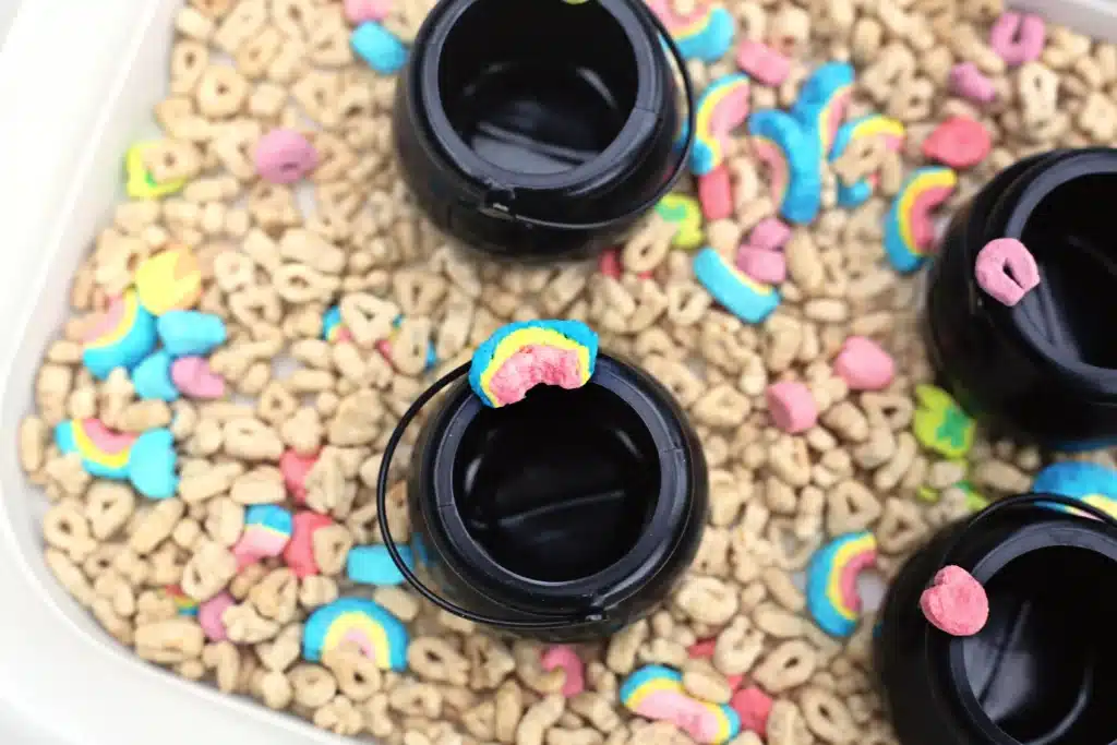 Lucky Charms Sensory Bin - Cultivating Brilliant Minds a sensory bin that uses lucky charms cereal, a scoop, and mini black cauldron pots