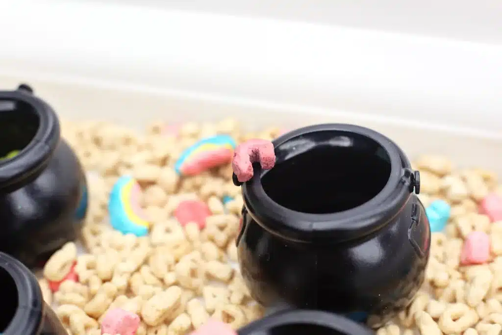 Lucky Charms Sensory Bin - Cultivating Brilliant Minds a sensory bin that uses lucky charms cereal, a scoop, and mini black cauldron pots