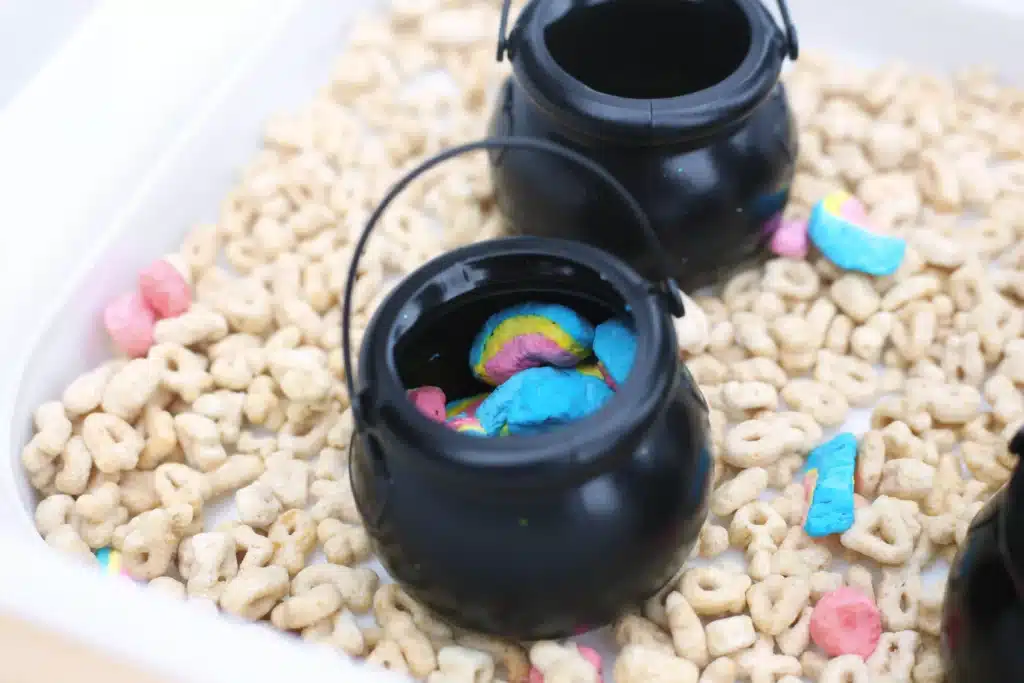 Lucky Charms Sensory Bin - Cultivating Brilliant Minds a sensory bin that uses lucky charms cereal, a scoop, and mini black cauldron pots