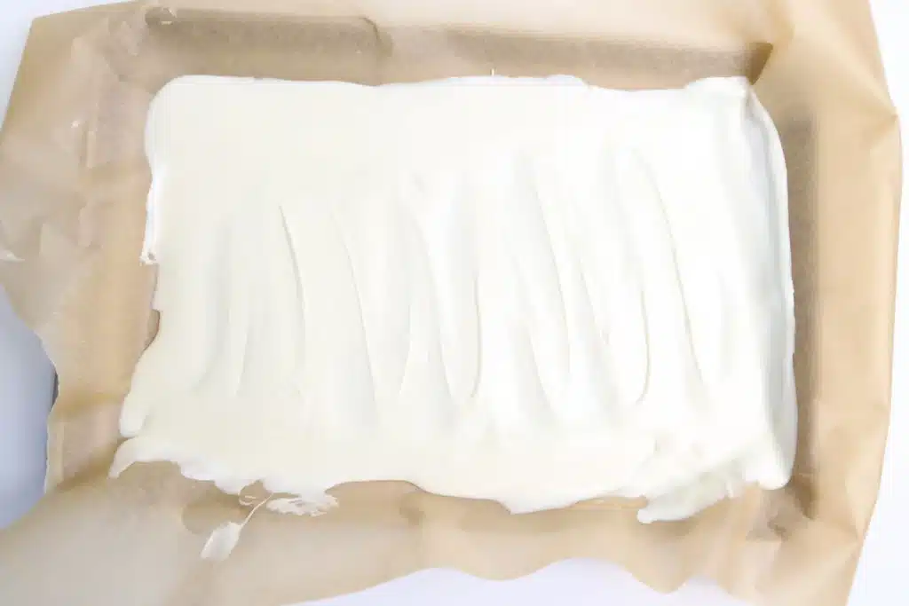 Lucky Charms Bark for St. Patrick's Day - Cultivating Brilliant Minds melted white chocolate spread on parchment paper