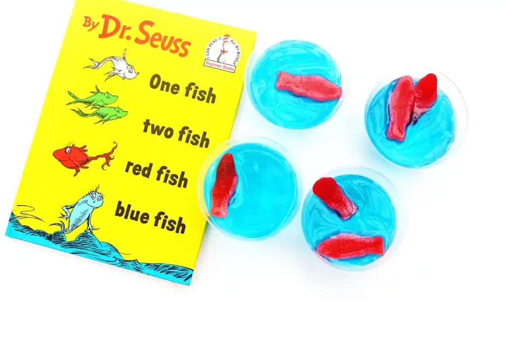 Dr. Seuss One Fish Two Fish Jello Cups - Cultivating Brilliant Minds blue jello cups with red swedish fish on top next to Dr. Seuss's One fish, two fish, red fish, blue fish book