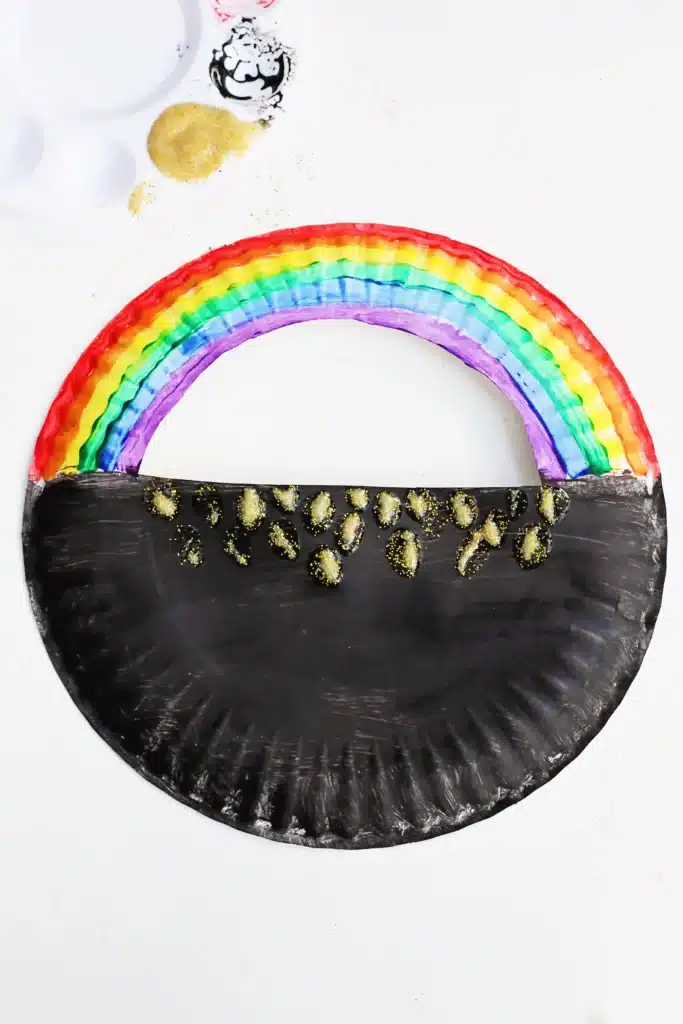 Paper Plate Pot of Gold with Fingerprint Coins - Cultivating Brilliant Minds a paper plate with a semi circle cut out of the top painted to look like a pot of gold with a rainbow on top