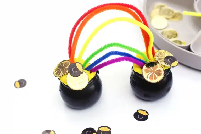 two black caludron pots with yellow playdough in each and rainbow color pipe cleaners sticking in each to create a rainbow