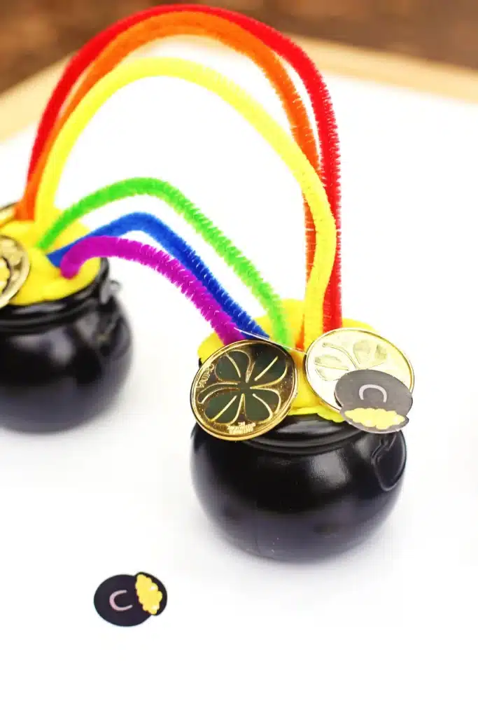 Pot of Gold Playdough Tray - Cultivating Brilliant Minds a black cauldron with yellow playdough inside and colored pipe cleaners stuck in the playdough to make a rainbow