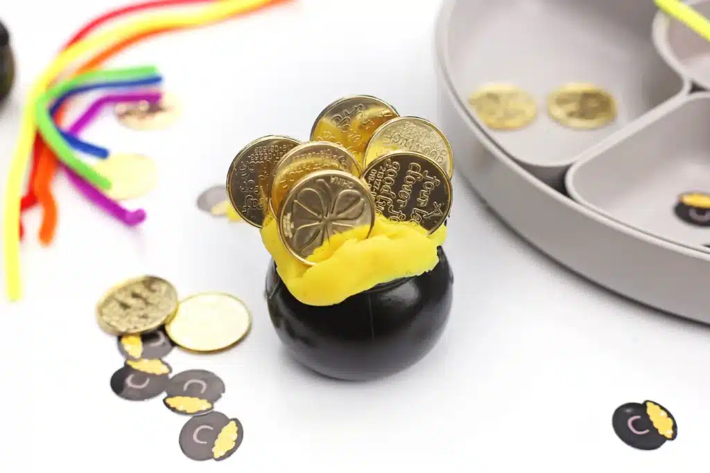 Pot of Gold Playdough Tray - Cultivating Brilliant Minds a black cauldron with yellow playdough inside and gold coins stuck in the playdough