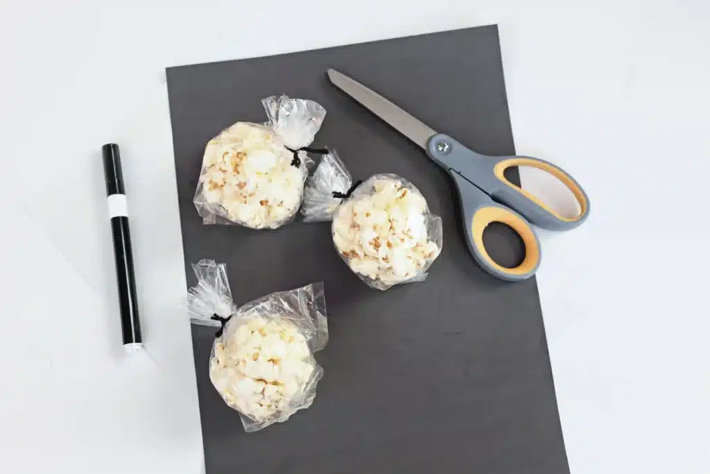 Sheep Popcorn Balls - Cultivating Brilliant Minds popcorn balls in bags, black marker, black construction paper, and scissors