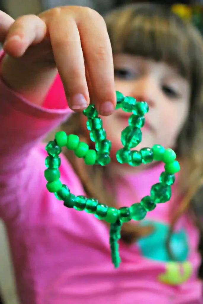St. Patrick's Day Crafts For Kids - Cultivating Brilliant Minds a green pipe cleaner bent into a shamrock with green beads on it