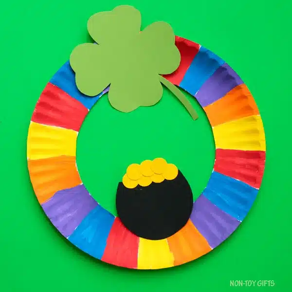St. Patrick's Day Paper Plate Crafts - Cultivating Brilliant Minds a paper plate painted like a rainbow with a shamrock and pot of gold glued on to make a wreath