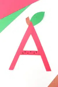 the letter a cut out of red construction paper with a leaf and stem glued on top