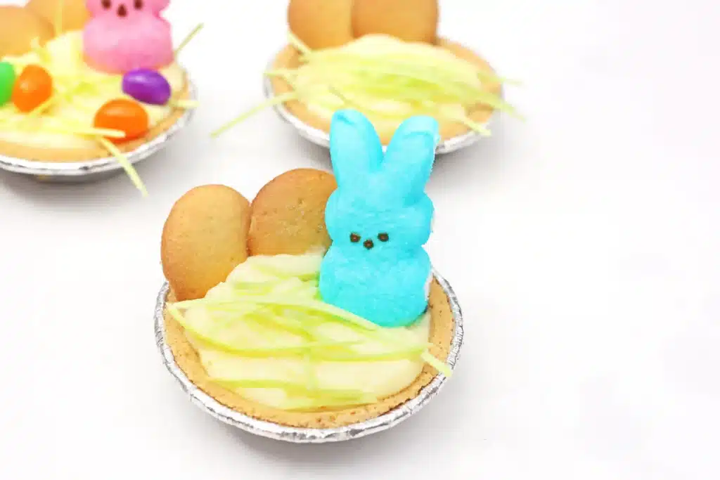 Peeps banana pudding mini pies - Cultivating Brilliant Minds a mini banana pudding pie with edible easter grass, nilla wafers, and a blue peeps bunny