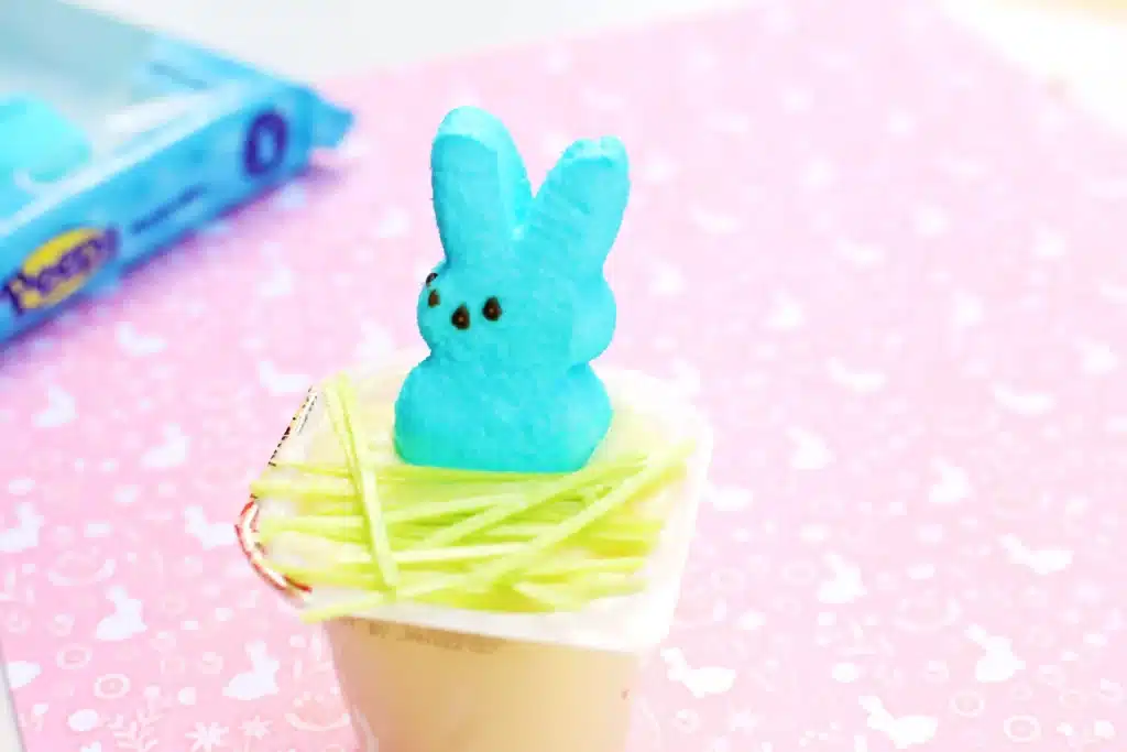 Easter Basket Pudding Cups - Cultivating Brilliant Minds a vanilla pudding cup with edible Easter grass and a blue peep on top