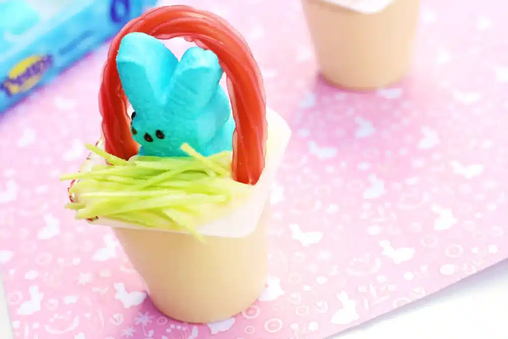 Easter Basket Pudding Cups - Cultivating Brilliant Minds a vanilla pudding cup with edible grass, a blue peep, and a twizzler bent to look like a handle