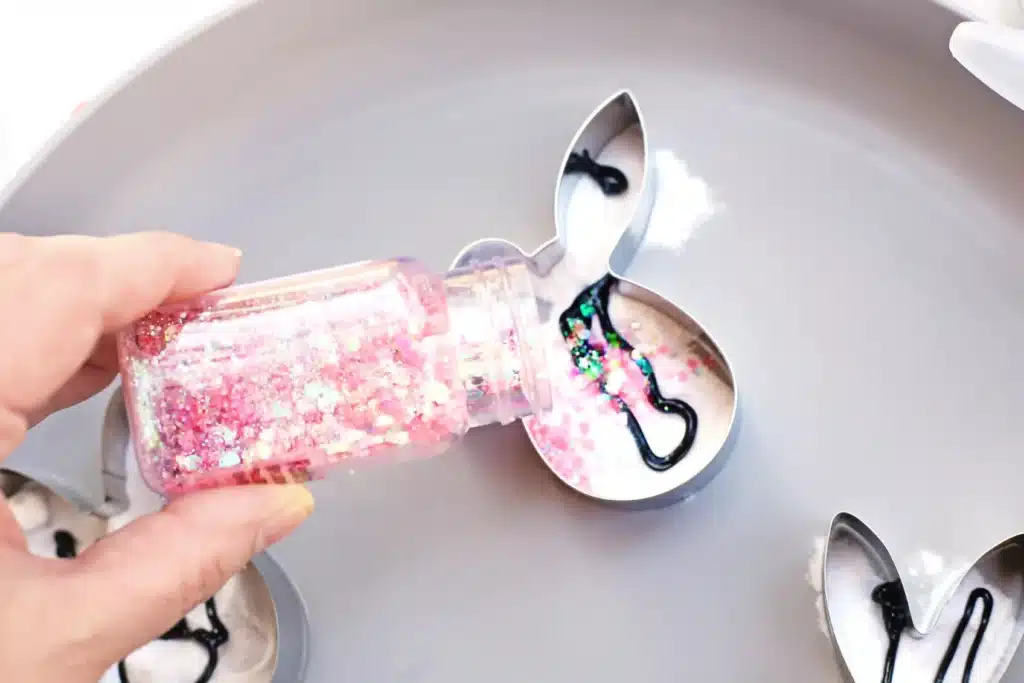 Fizzy Bunny Experiment - Cultivating Brilliant Minds adding glitter to the baking soda and food coloring in a bunny cookie cutter