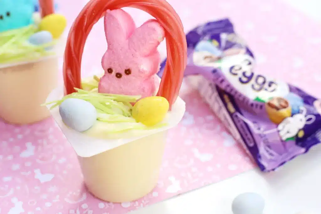 Easter Basket Pudding Cups - Cultivating Brilliant Minds a vanilla pudding cup with edible grass, cadbury mini eggs, a peep, and a twizzler bent to look like a handle