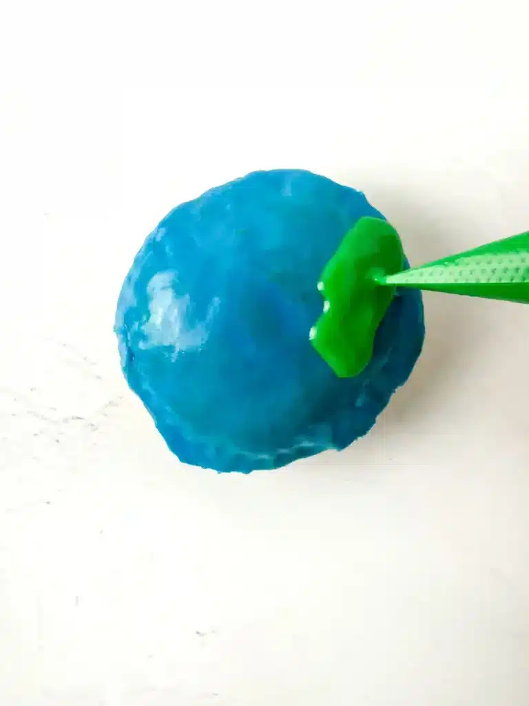 Blueberry Earth Day Hand Pies - Cultivating Brilliant Minds piping green icing on top of the blue icing on a hand pie