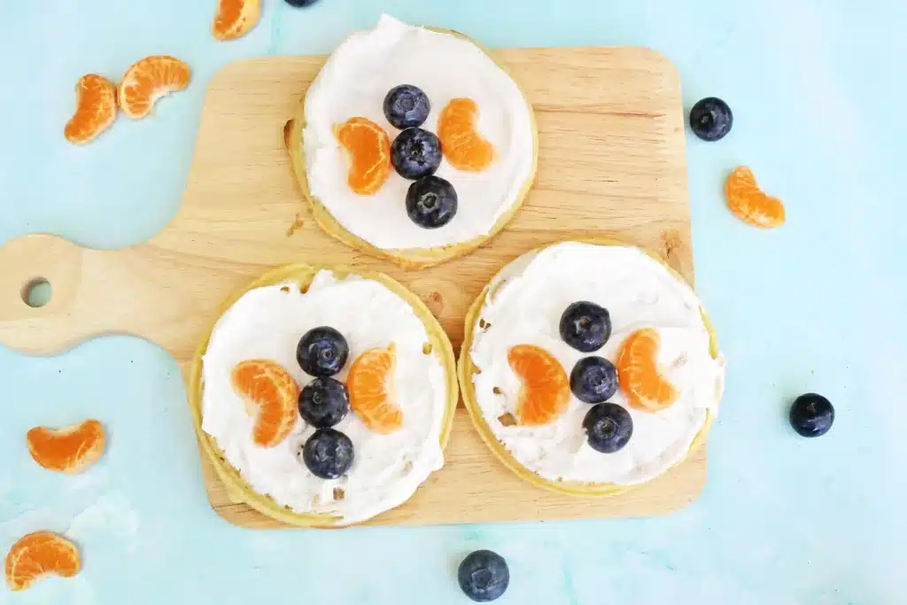Butterfly Garden Waffles: A Spring Breakfast Idea For Kids - Cultivating Brilliant Minds waffles with whipped cream and blueberries and oranges arranged to look like a butterfly
