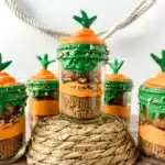 a jar with two cupcakes in it with orange and green icing to look like a carrot