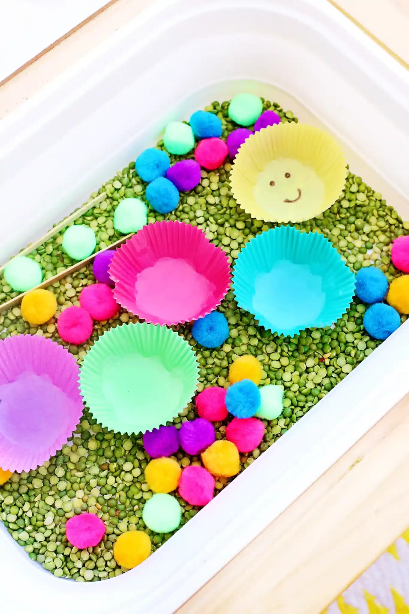a spring color sorting sensory bin with green split peas, colored cupcale liners, and pom poms