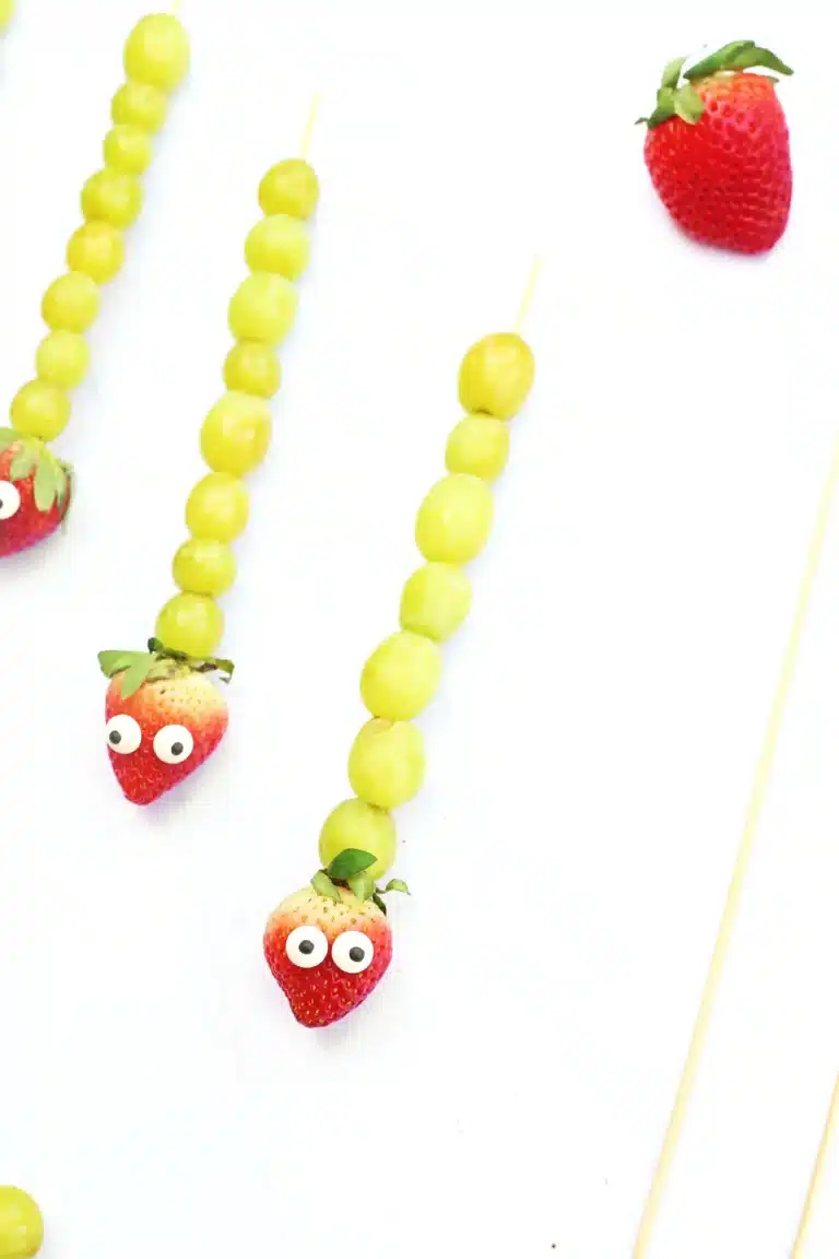 skewers with grapes, a strawberry, and candy eyes on it to look like a caterpillar