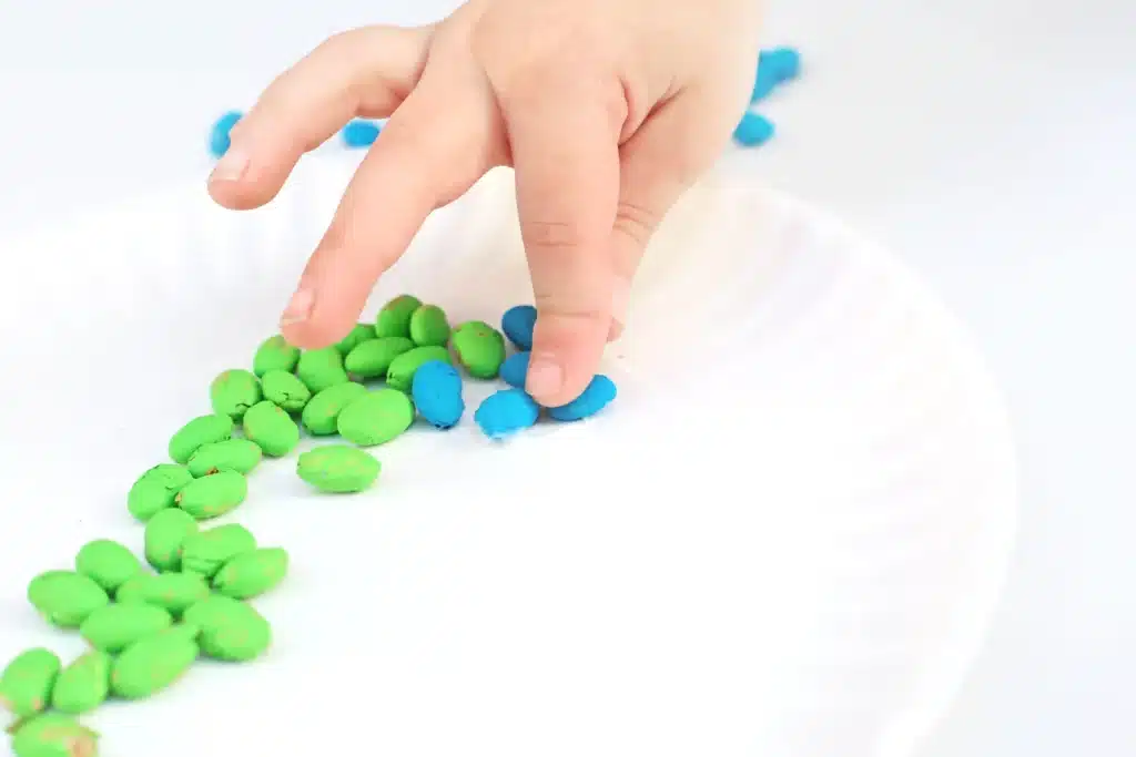 Bean Earth Day Mosaic - Cultivating Brilliant Minds a kid glueing blue dyed pinto beans to a paper plate