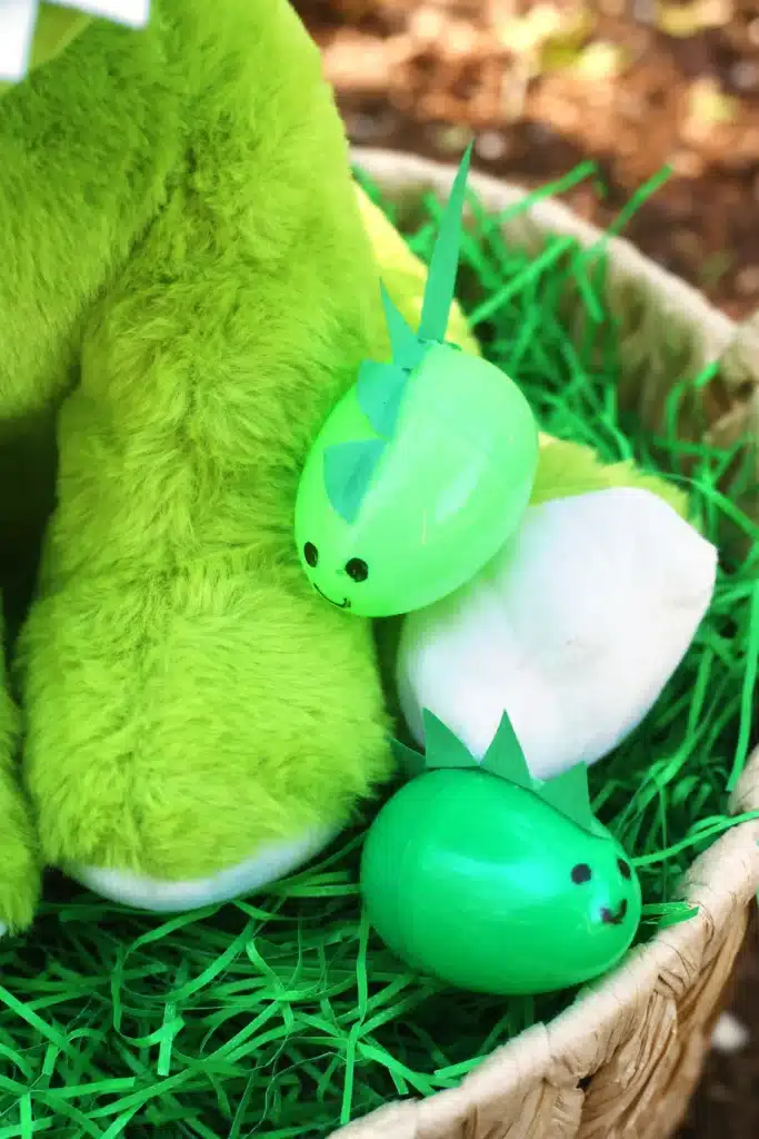 Dinosaur Easter Basket For Kids - Cultivating Brilliant Minds an easter basket with a dinosaur plush and green easter eggs decorated to look like dinosaurs