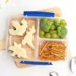 Dinosaur Lunch Idea - Cultivating Brilliant Minds a lunchbox with sandwiches cut into dinosaurs, pretzels, broccoli, and green grapes