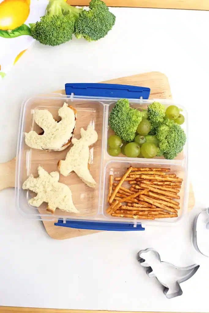 Dinosaur Lunch Idea - Cultivating Brilliant Minds a lunchbox with sandwiches cut into dinosaurs, pretzels, broccoli, and green grapes