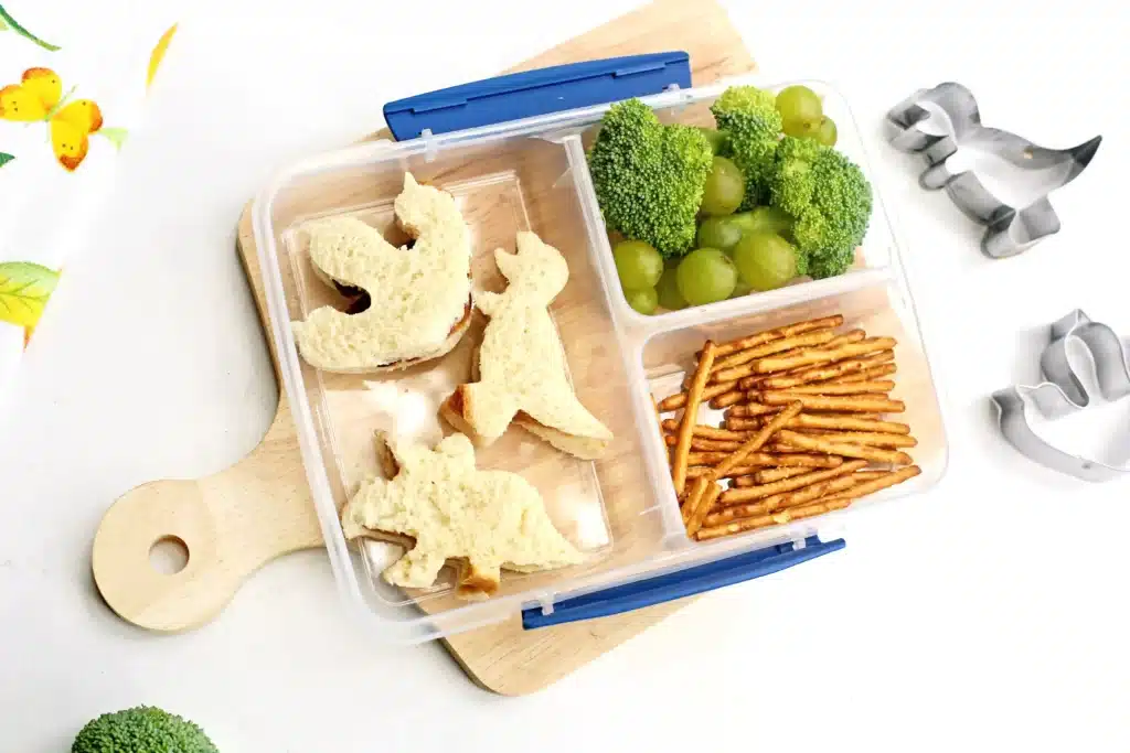 Dinosaur Lunch Idea - Cultivating Brilliant Minds a lunchbox with sandwiches cut into dinosaurs, pretzels, broccoli, and green grapes