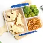Dinosaur Lunch Idea - Cultivating Brilliant Minds a lunchbox with sandwiches cut into dinosaurs, pretzels, broccoli, and green grapes